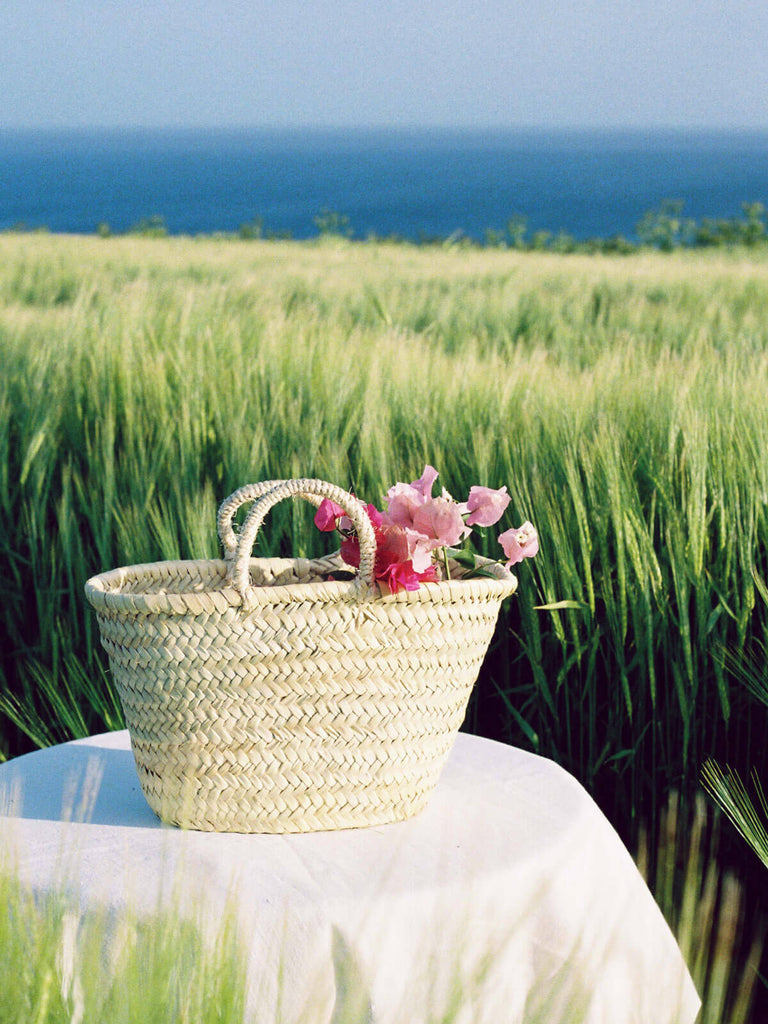 A small natural woven Market Basket filled with flowers by the sea
