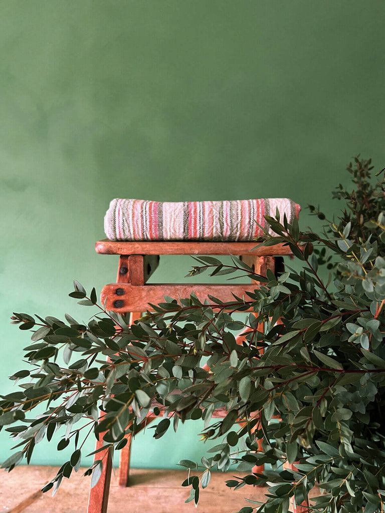 Pink striped hammam towel on a rustic stool with foliage
