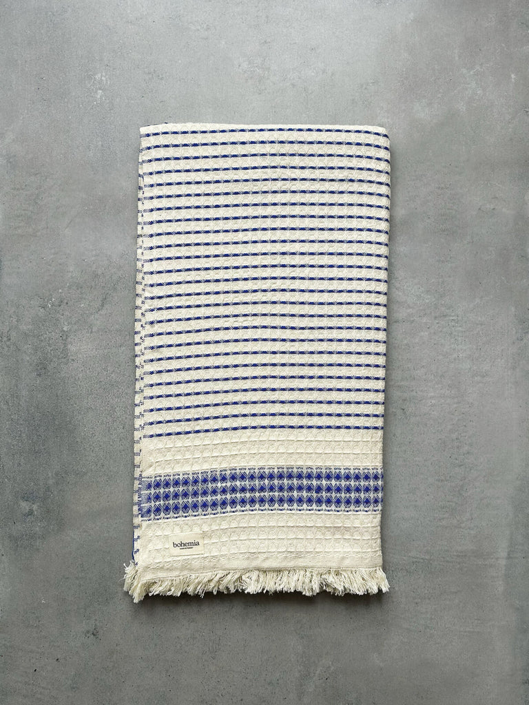 Soft Turkish cotton hammam towel in blue, featuring a subtle waffle textured weave, displayed against a textured grey background by Bohemia Design