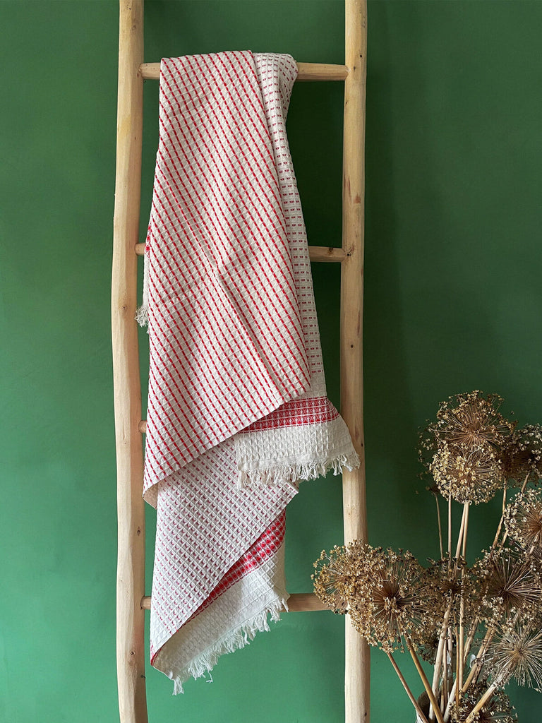 Made from premium Turkish cotton, the Milos Hammam Towel with fine terracotta stripes and delicate hand-tied tassel fringe, displayed on a rustic wooden ladder | Bohemia Design