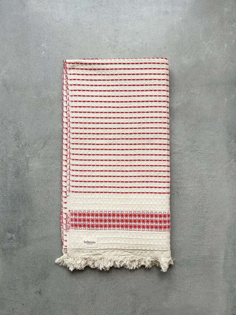 Milos Hammam Towel with a waffle texture and a subtle terracotta striped pattern, presented on a grey textured background