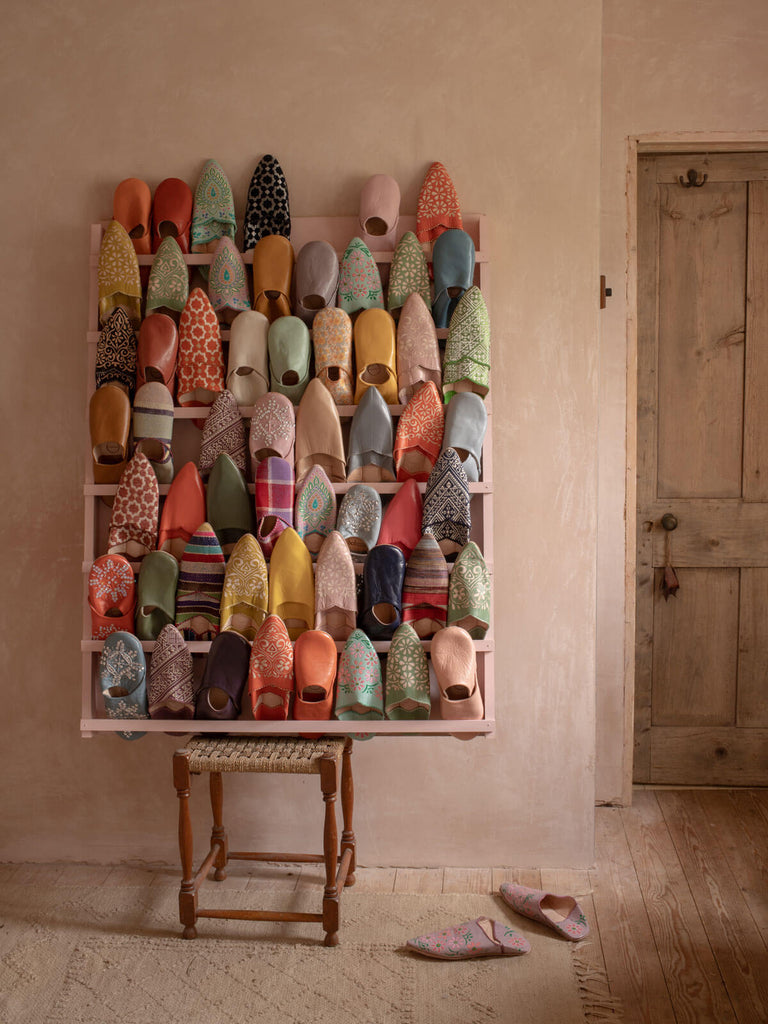 A display of many styles of Moroccan Babouche slippers by Bohemia Design in a plaster pink room