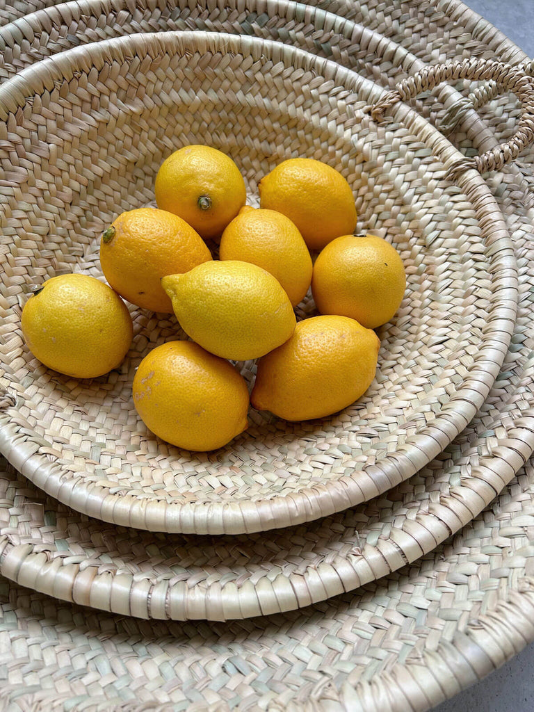 Group of woven plates holding lemons, crafted from natural palm leaf by Moroccan artisans.
