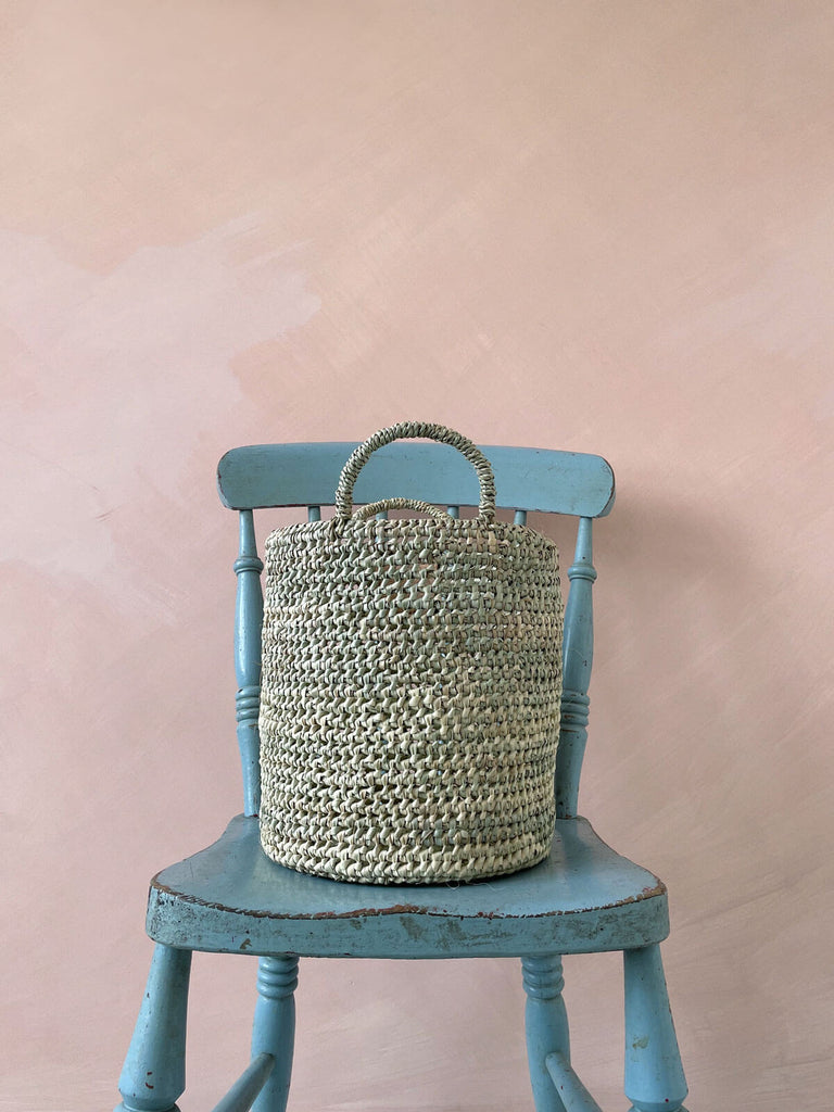 Large open weave nesting basket on a blue chair in front of a pink wall