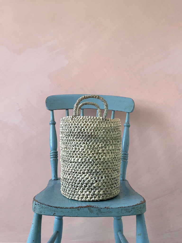 Medium open weave nesting basket on a blue chair in front of a pink wall
