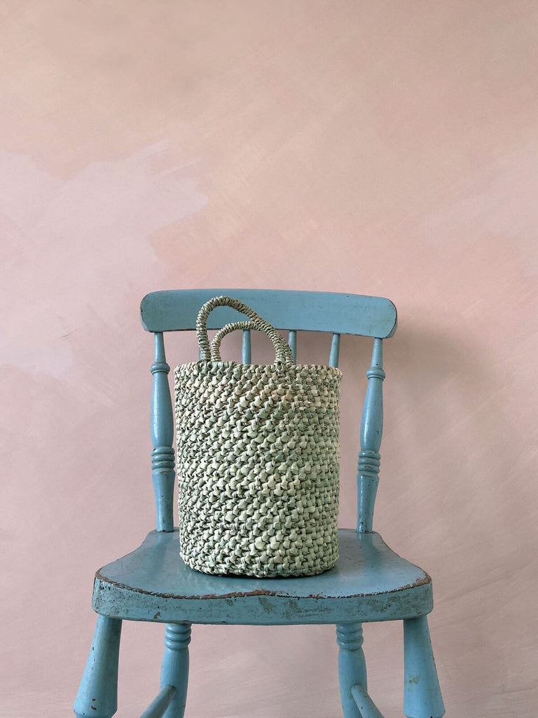 Small open weave nesting basket on a blue chair in front of a pink wall