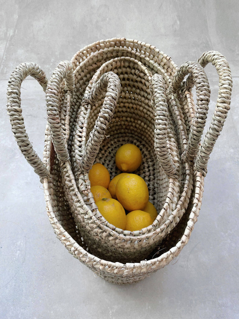 Three oval handwoven shopping or storage basket bags nesting inside each other with lemons