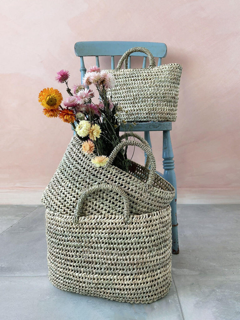 Set of three different sizes of natural woven open weave straw storage baskets with dried flowers