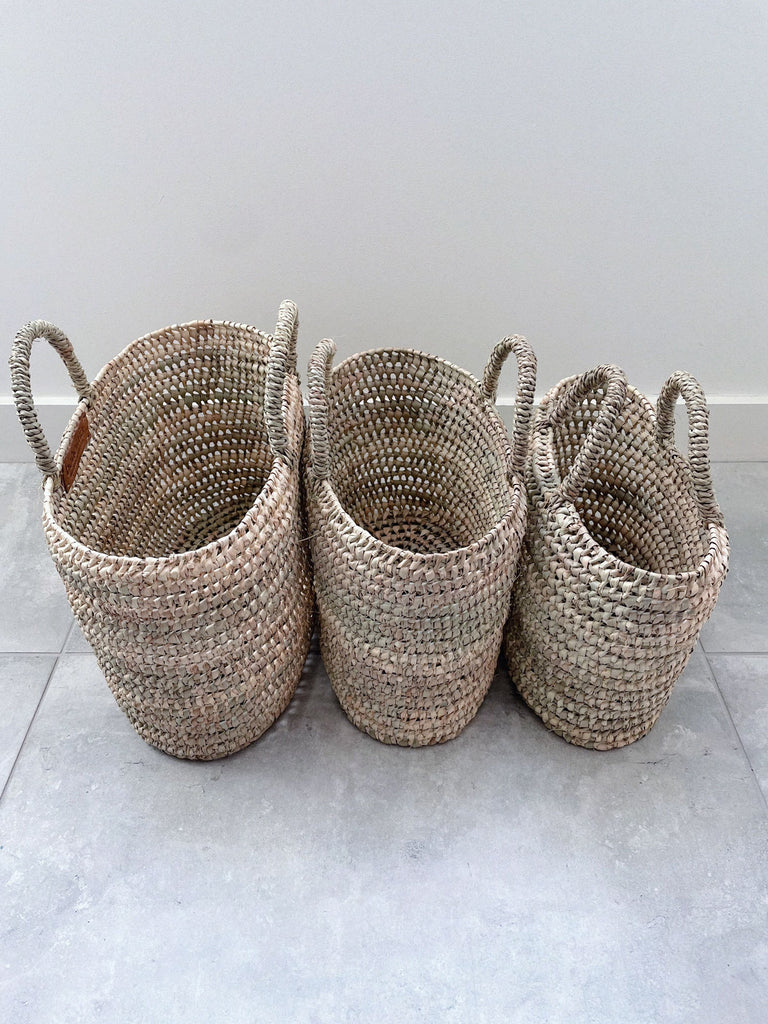 Three sizes of handwoven oval shaped nesting basket bags with open weave design and short handles