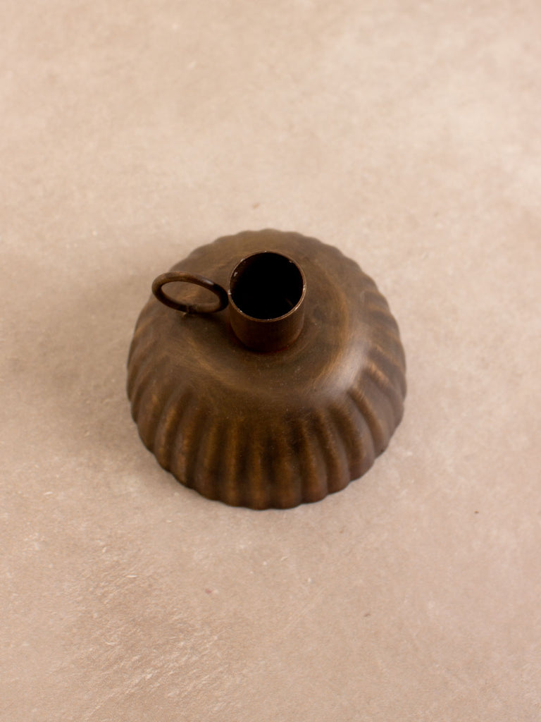 A metal candle holder with petticoat shape and finger hold