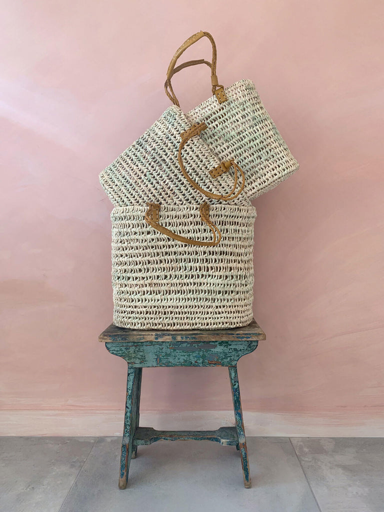 Three pleated leather handle baskets on a blue vintage side table in front of a pink wall