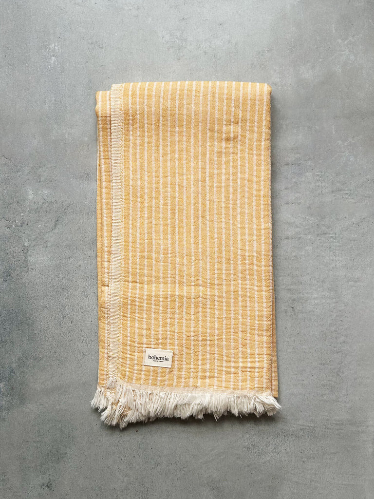Soft Turkish hammam towel in mustard yellow with subtle woven stripes, set against a  textured grey background | Bohemia Design