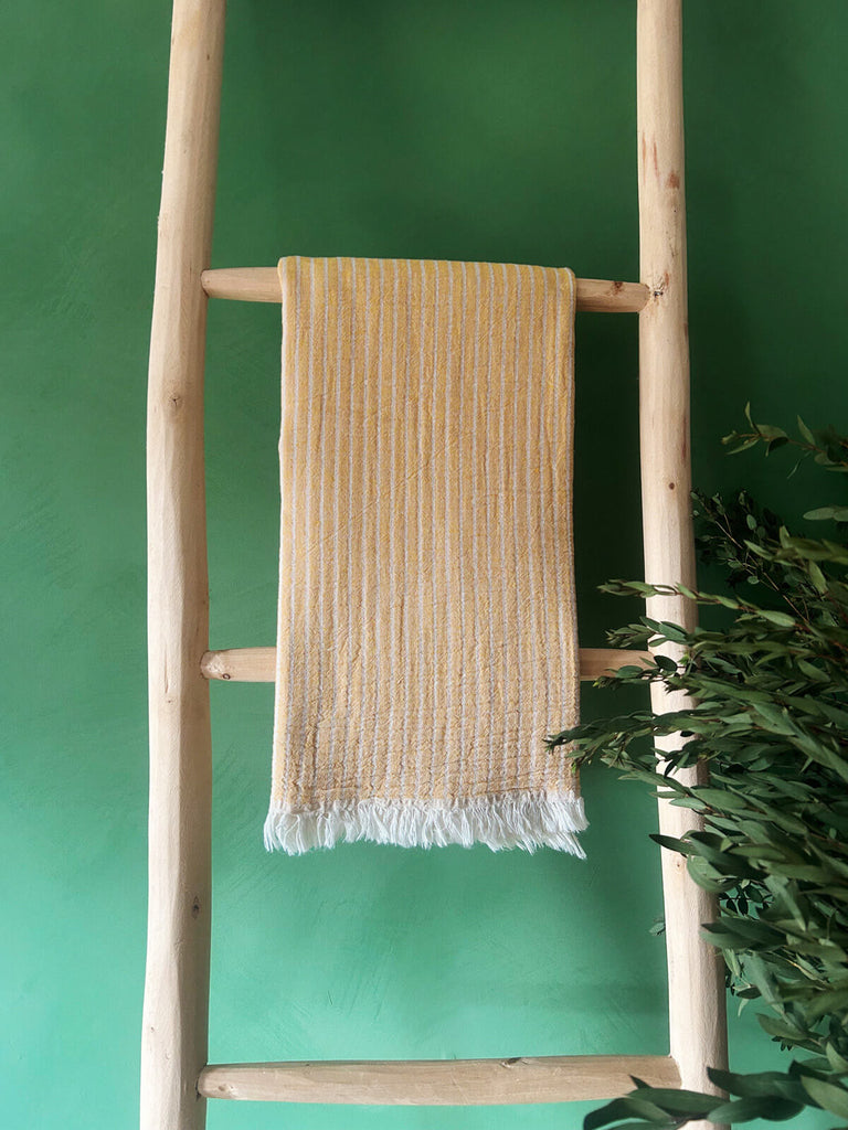 Soft cotton Portobello Hammam Towel in mustard yellow with subtle woven stripes, presented on a rustic wooden ladder | Bohemia Design
