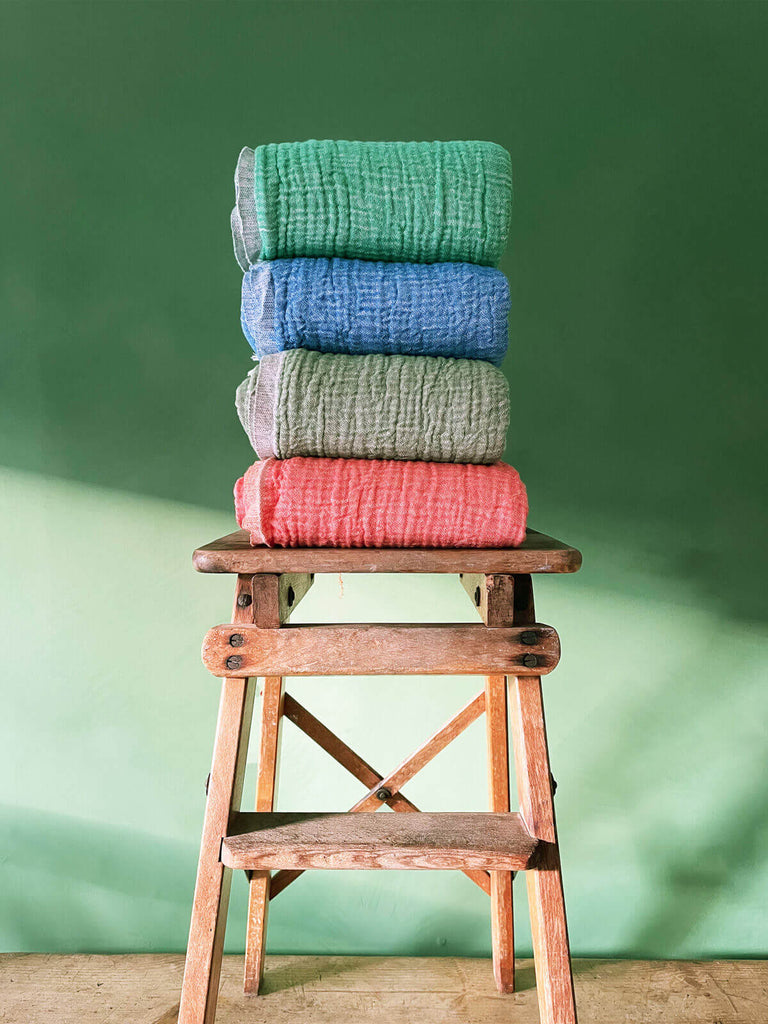 Soft cotton Samos hammam towels in four colourways folded on a wooden stool