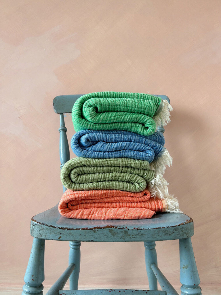 Pile of Samos hammam towels in different colours folded on a wooden chair | Bohemia Design