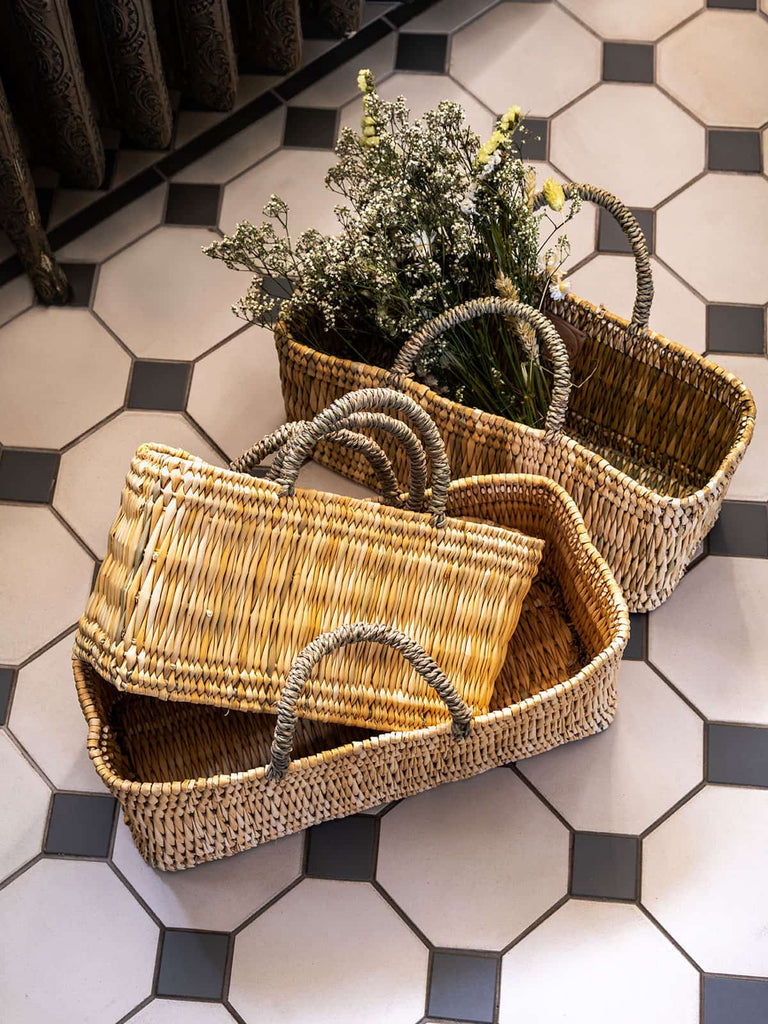 Two traditional Moroccan woven reed wicker storage baskets holding dried flowers on a tiled floor. 