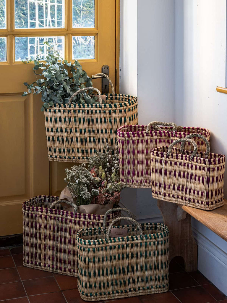 A collection of colourful woven reed basket bags with dried flowers in a hallway