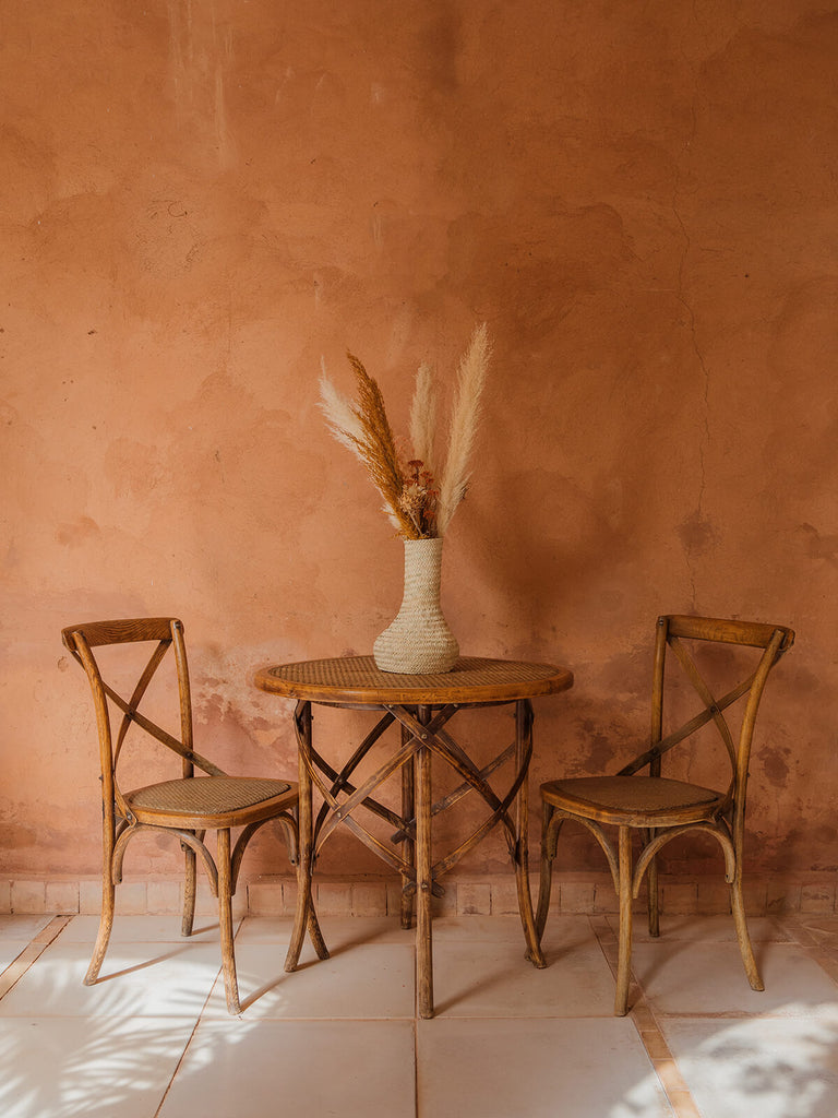 Bohemia design palm leaf basket vase on a wooden table with two chairs against a terracotta wall
