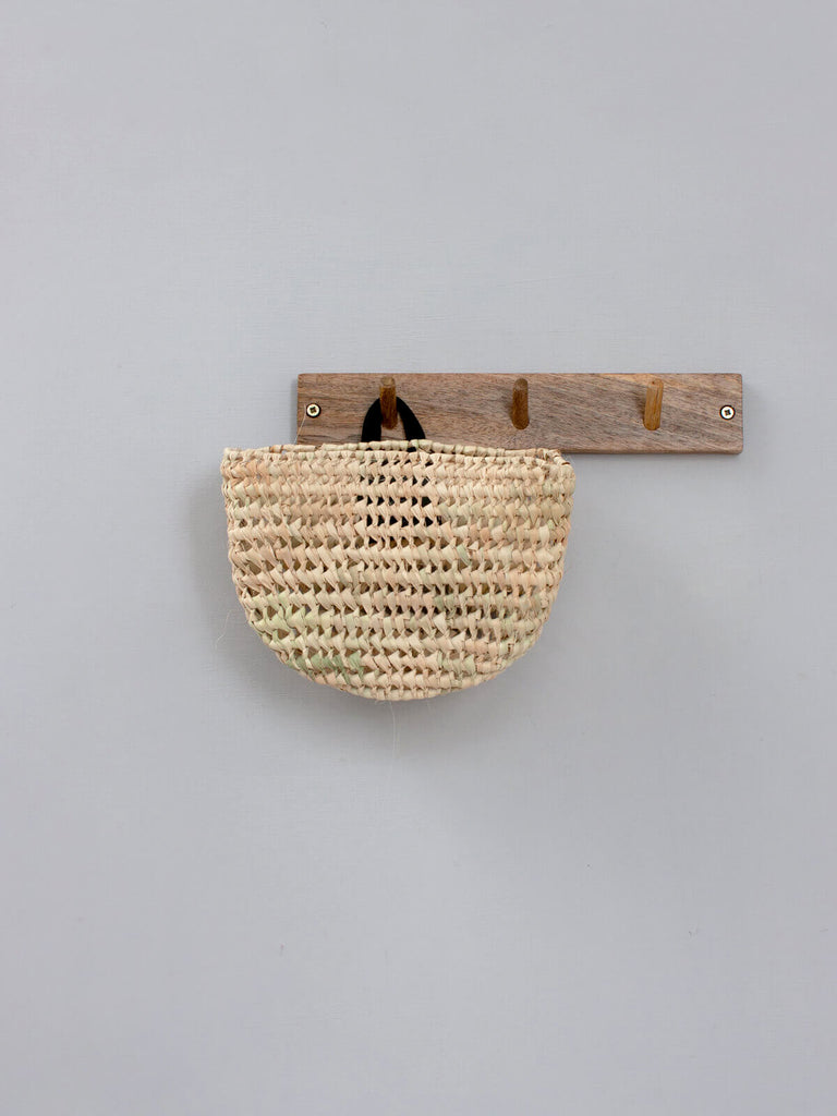 Natural woven mini wall basket with black leather loop hanging on a wooden hook