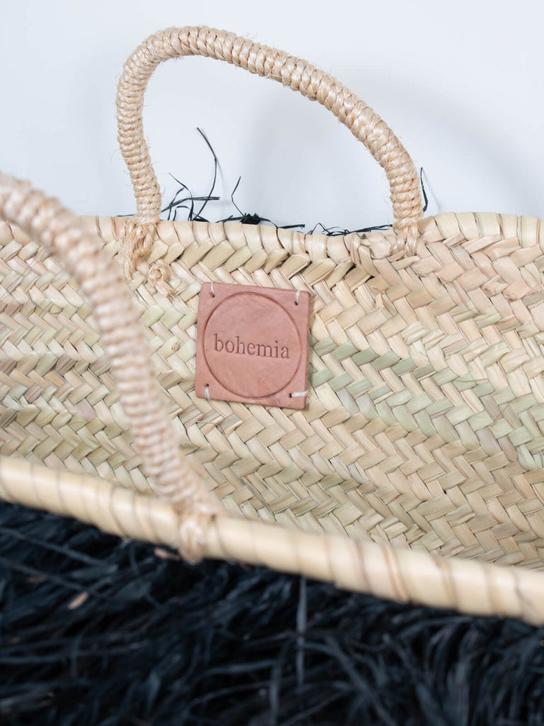 Close up of the short handled Raffia Tassel Basket and the branded leather Bohemia label inside