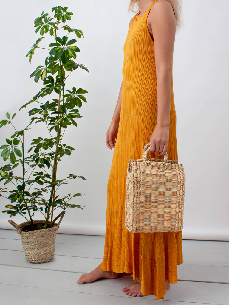 Model holding a natural reed box basket bag with short sturdy handles