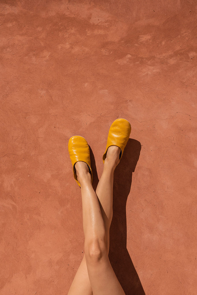 Bohemia-design-Moroccan-leather-babouche-slippers-mustard-model-against-terracotta-wall