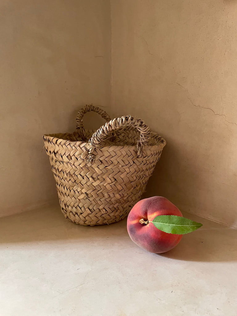 Tiny beldi basket by Bohemia Design against a neutral wall with a peach
