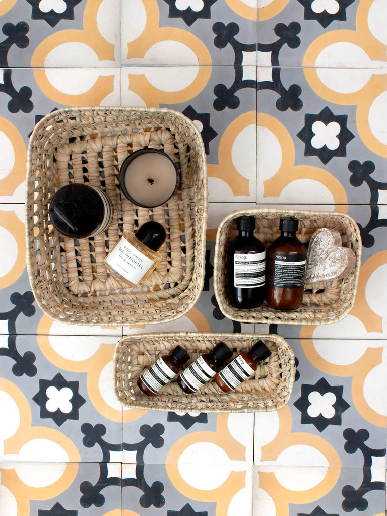 Three sizes of natural woven storage basket trays used to organise bathroom beauty essentials and toiletries