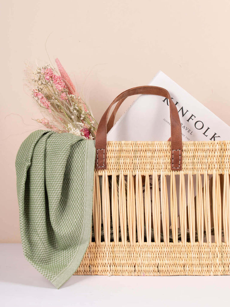 Natural decorative reed basket filled with a bunch of dried flowers, scarf and magazine