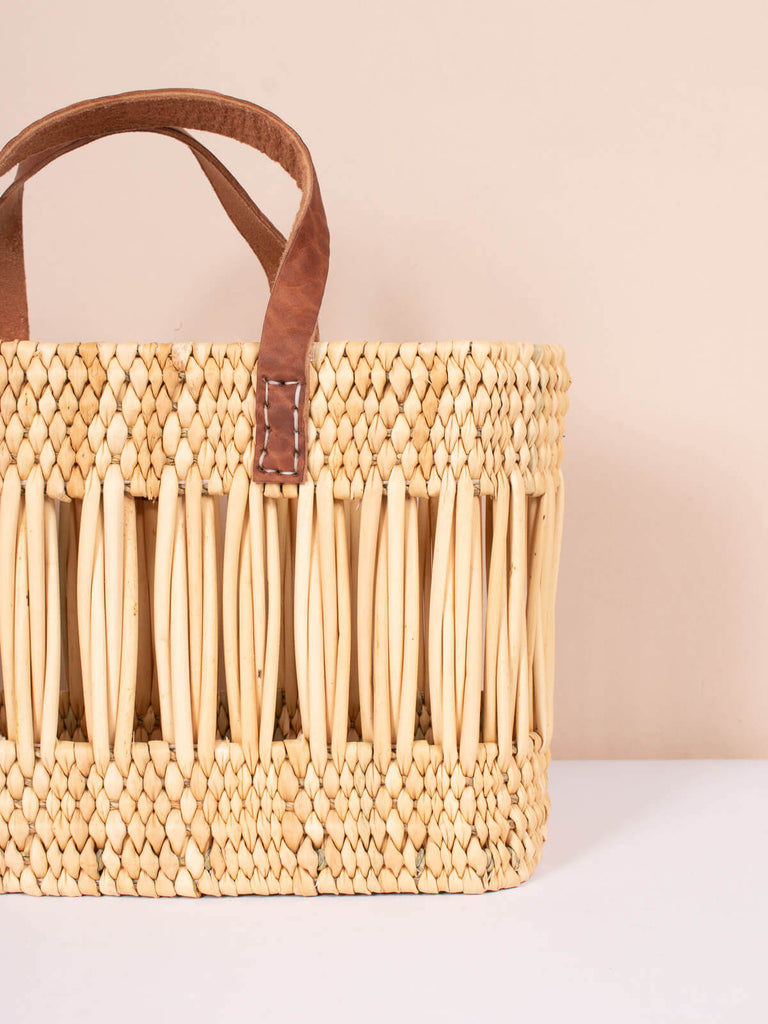 Rectangular reed basket bag with decorative open weave design and leather handles