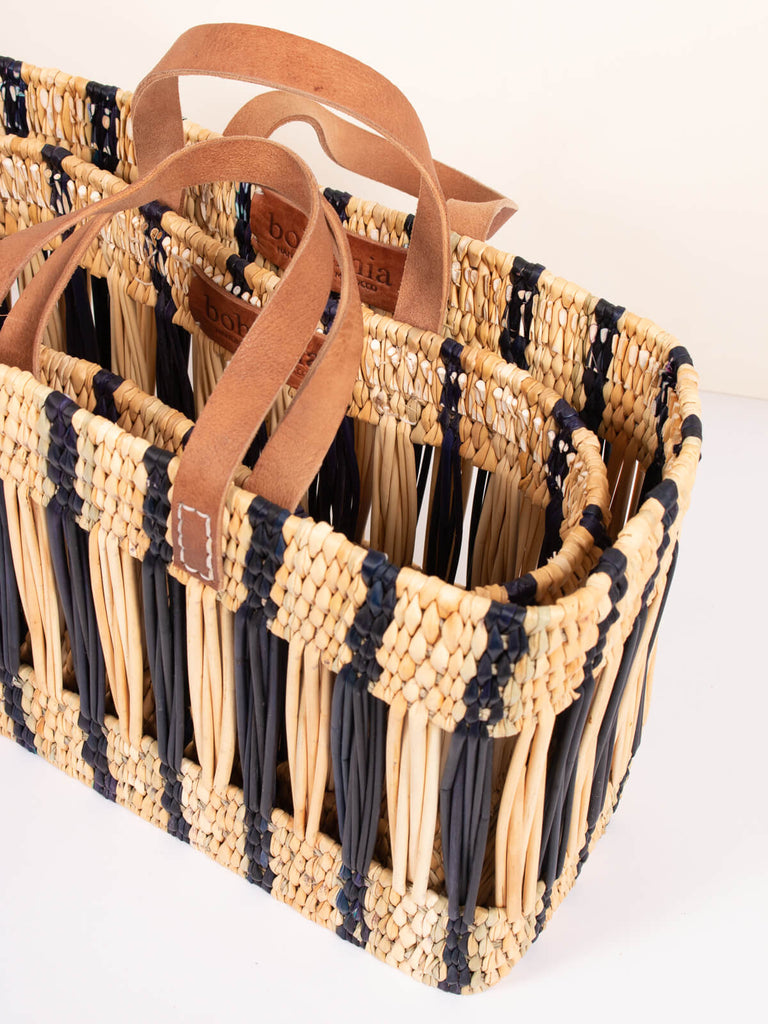Two nesting decorative woven reed baskets with indigo stripes, leather handles and hand stamped leather Bohemia label