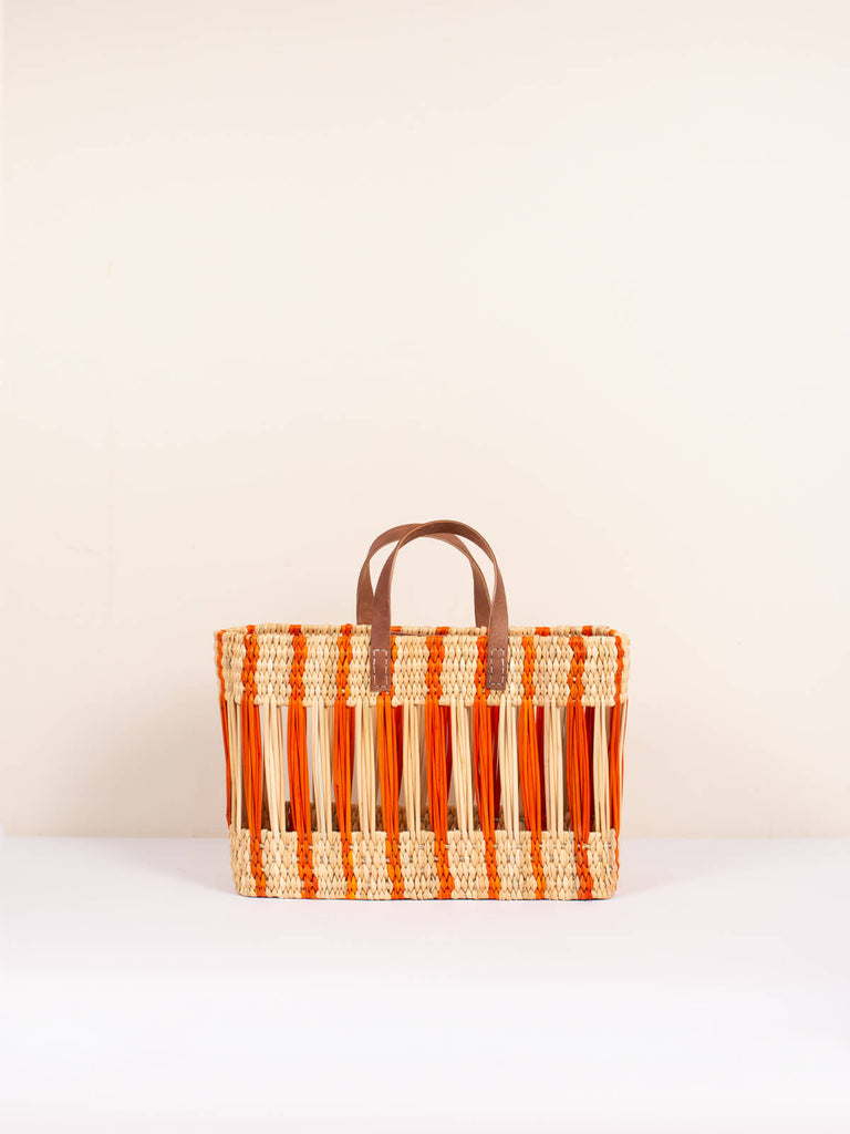 Small, boxy, decorative reed woven basket bag with orange stripe design and leather handles