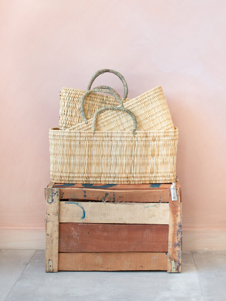 Three sizes of hand woven Moroccan natural reed wicker storage baskets on a wood crate