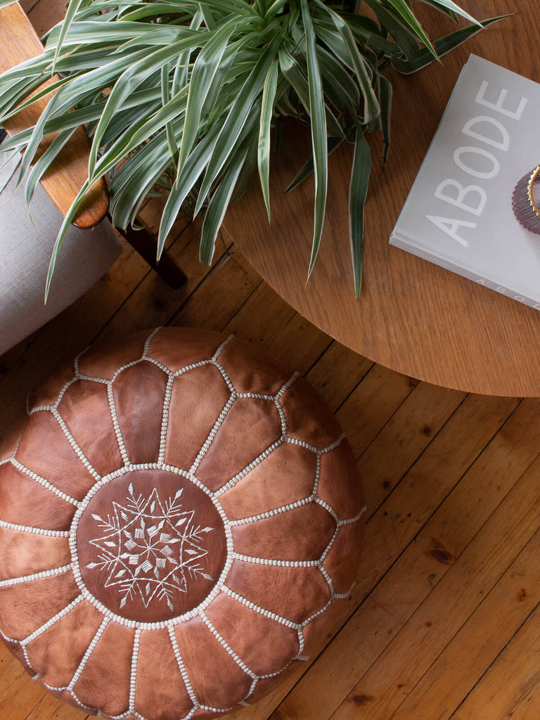 Moroccan Leather Pouffe, Chestnut beside a low coffee table and plant