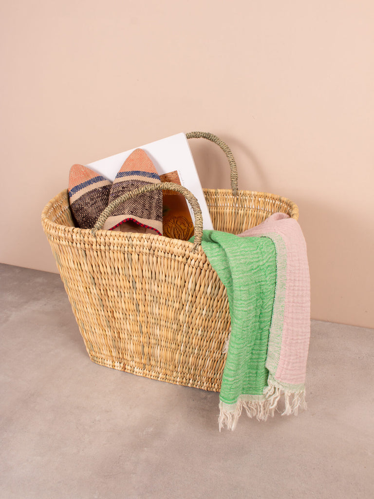 Natural handwoven sturdy reed shopper basket holding a scarf, slippers and magazine