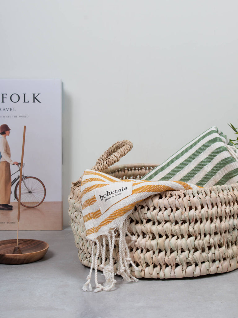 Round open weave natural storage basket with textiles and a magazine
