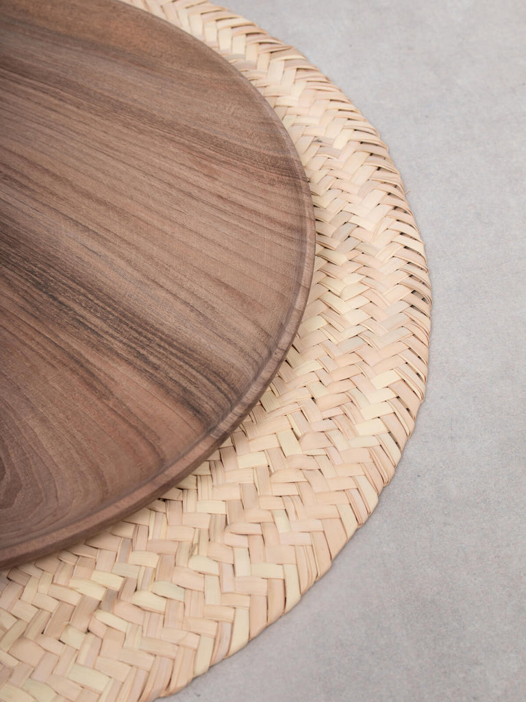 A Walnut Wood Plate on top of a natural palm leaf placemat.