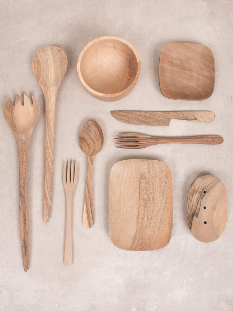 A flat lay of various walnut wood tableware including a pair of salad servers