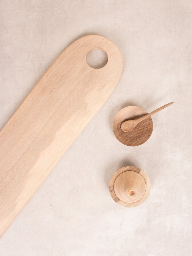 Long walnut wood serving board next to small spice bowl and spoon