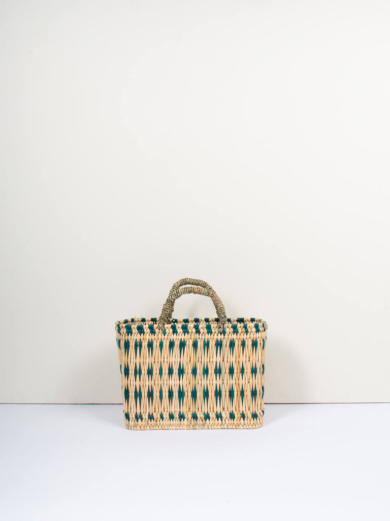 Small boxy woven reed basket bag with handles and skillfully weaved green pattern by Bohemia Design