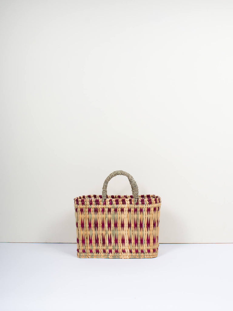 Small natural woven rectangular reed basket bag with short handles and featuring a skillfully weaved violet pattern
