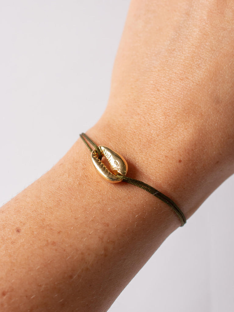Woman wearing gold cowrie bracelet with olive silk thread by Bohemia Design