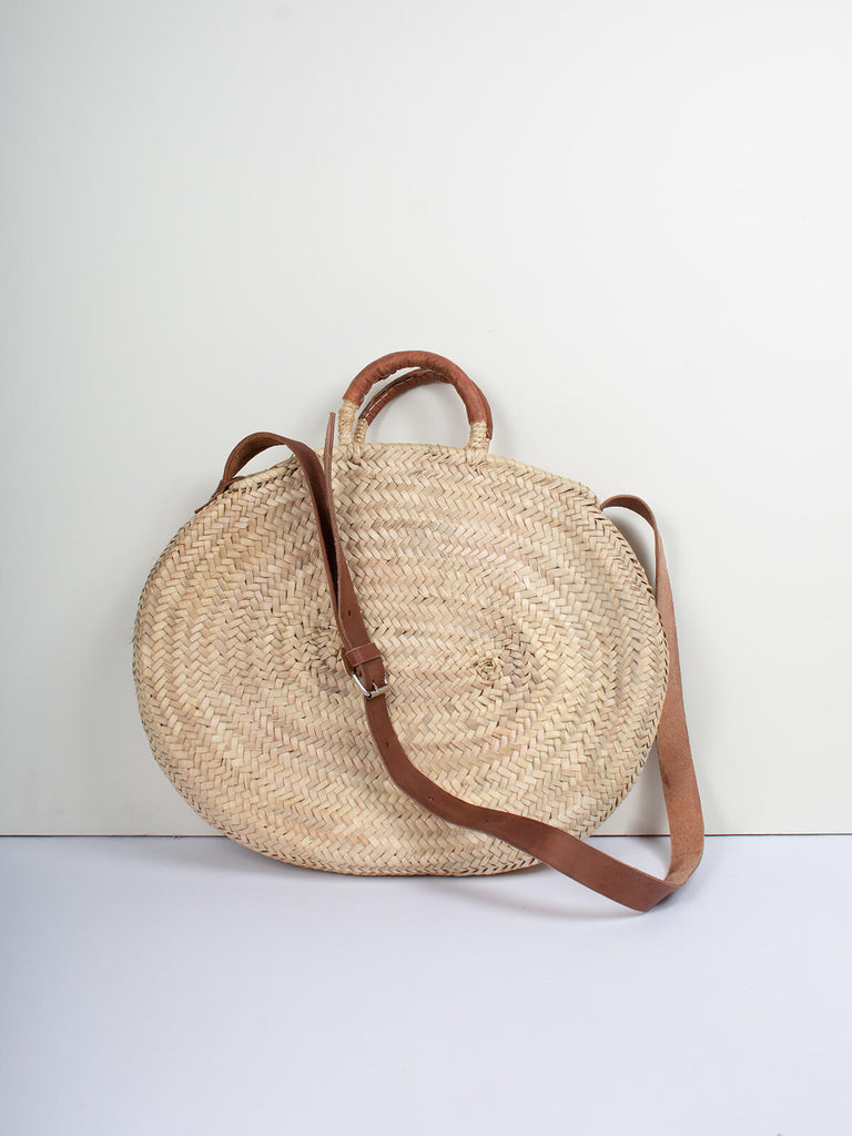 Moroccan woven basket in an oval shape with tan leather strap and handles by Bohemia Design