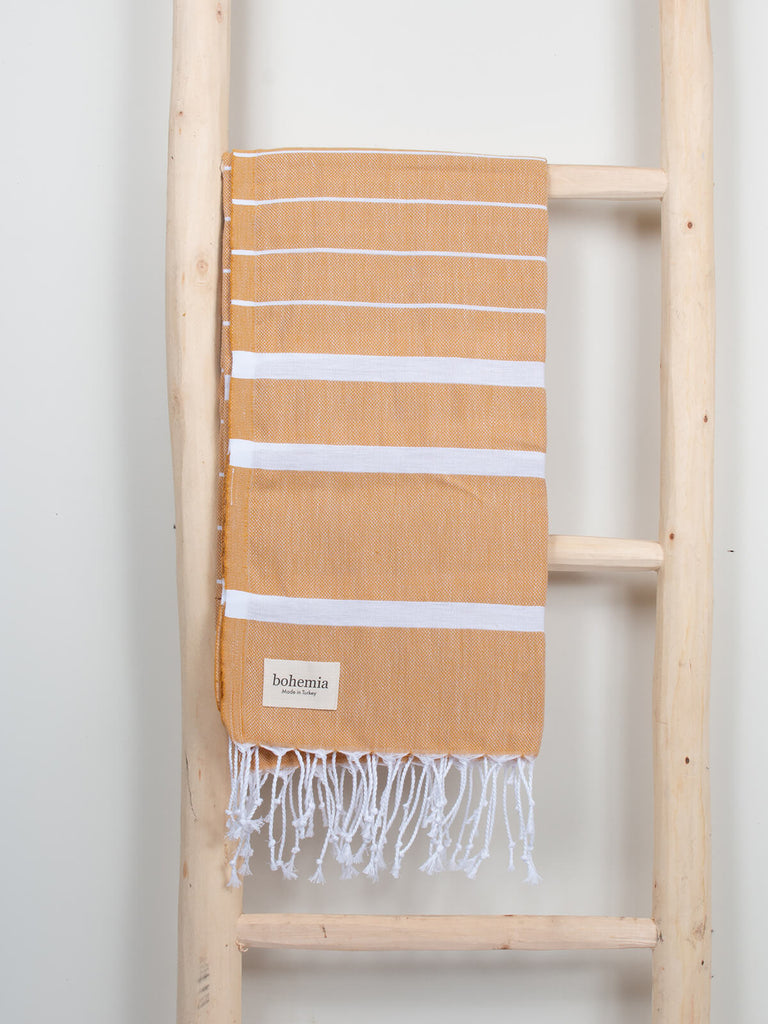 Ibiza Summer Hammam Towel in mustard stripe pattern by Bohemia Design hanging on a wooden ladder