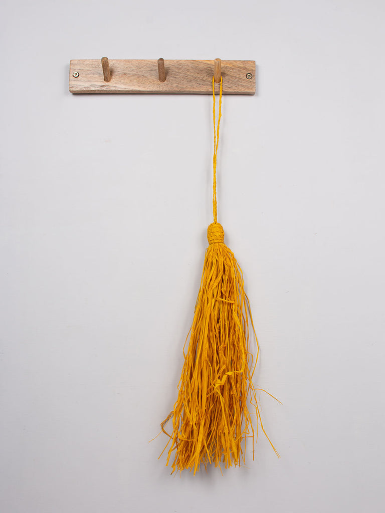 Mustard raffia tassel hanging on a wooden hook