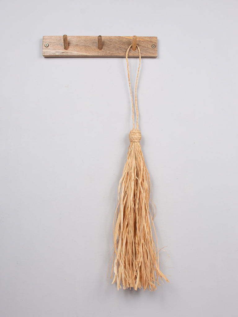 Natural raffia tassel hanging on a wooden hook