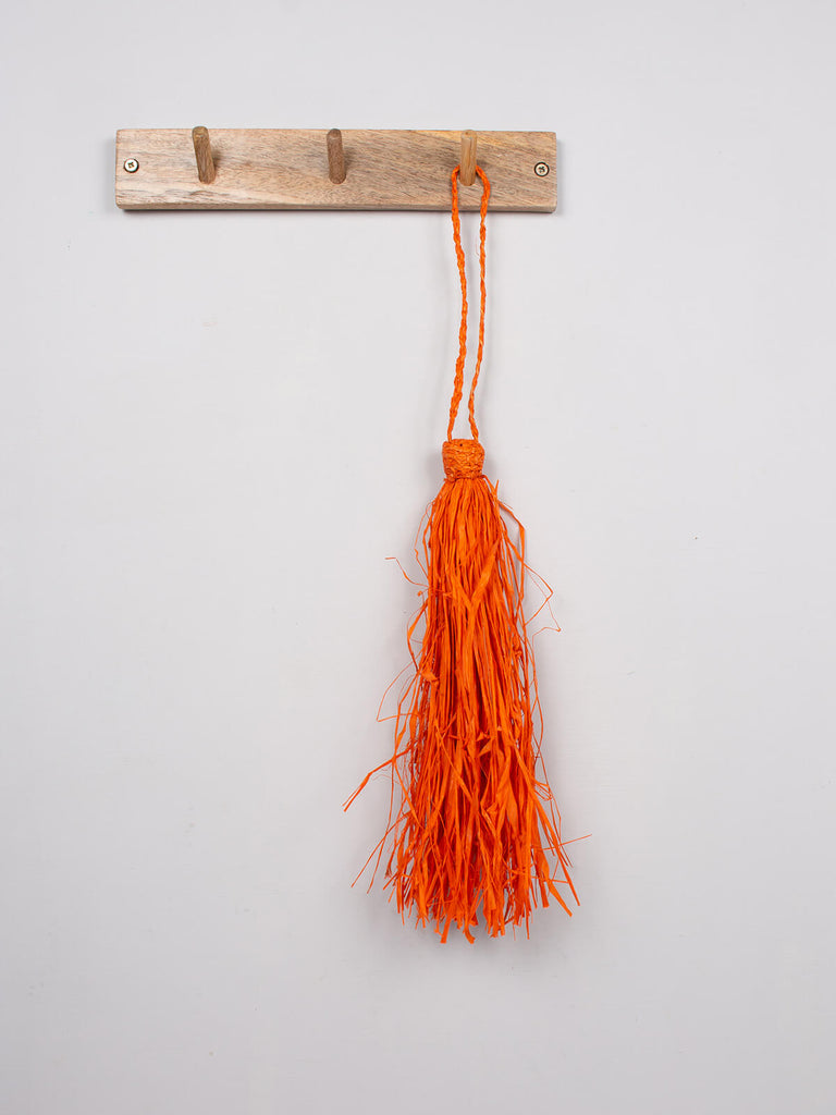 Orange raffia tassel hanging on a wooden hook