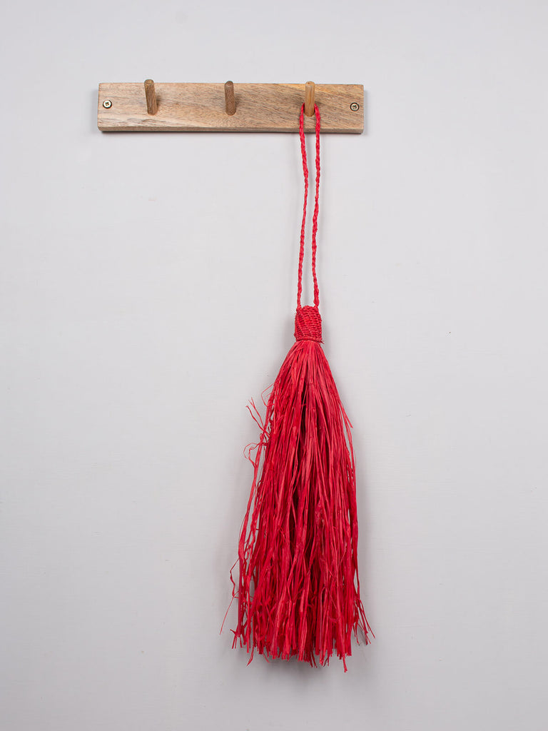 Red raffia tassel hanging on a wooden hook