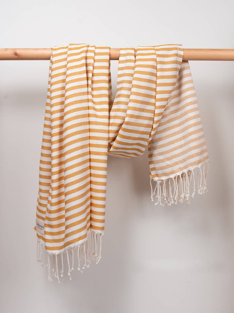Striped Sorrento Hammam Towel in mustard stripe by Bohemia Design hanging from a wooden rod