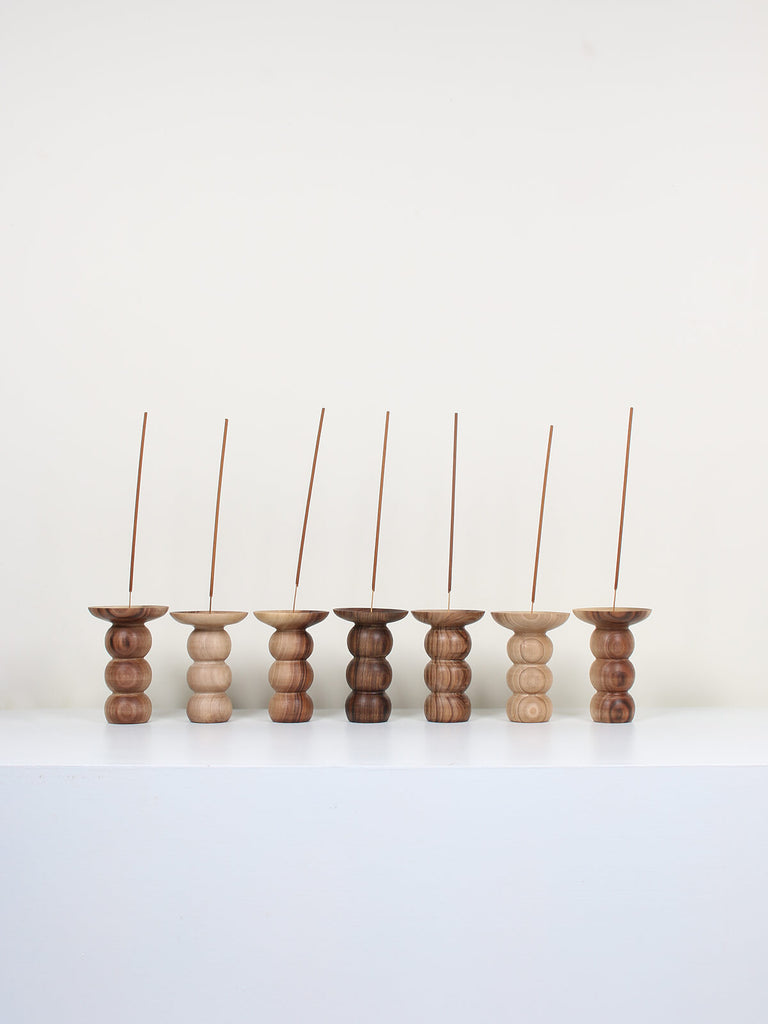 A group of natural walnut wood incense holders in a stacked bubble shape with sticks of incense 